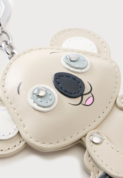 Porte-clés en cuir beige en forme de visage d'ours avec des yeux, un nez et une bouche souriante cousus.