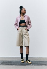 Ljusrosa texturerad skjorta, svart crop top, beige knälånga shorts, svarta strumpor och guldiga sportskor med svarta detaljer.