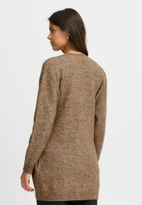 Maglione marrone lavorato a maglia con maniche lunghe, orlo a coste e tasche laterali. Texture morbida e vestibilità rilassata, vista dal retro, con dettagli minimi.