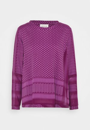 Fioletowa bluzka z długim rękawem z różnymi wzorami, w tym geometrycznymi i poziomymi paskami. Okrągły dekolt i luźny krój.