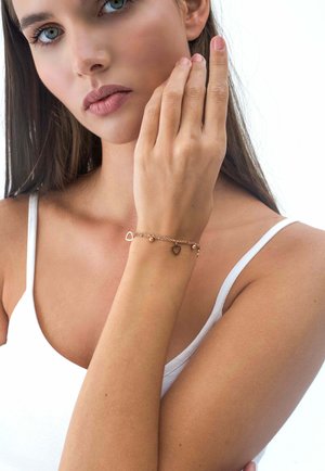 Braccialetto in oro rosa con ciondoli a forma di cuore e perline decorative, caratterizzato da un design di catena delicata. Indossato su un polso con pelle chiara.