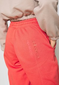 Coral sweatpants with an elastic waistband, side pockets, and embroidered "adidas" logo in matching color on the thigh.