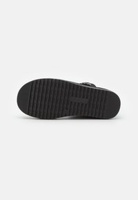 Suola di scarpa in gomma nera con scanalature orizzontali e marchio. Presenta una superficie uniforme e strutturata per aderenza e durata.