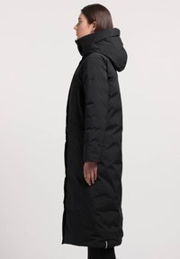 Sort lang pufferjakke med hætte, med en sidelomme og et enkelt, strømlinet design. Fremstillet af isolerende, vandafvisende materiale.