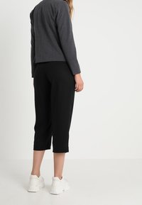 Blazer grigio corto con un design strutturato, abbinato a pantaloni neri alla caviglia e sneakers bianche chunky, mostrato da dietro.