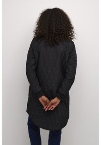 Schwarzer, gesteppter Langmantel mit abgerundetem Saum, langen Ärmeln und gerippten Bündchen. Das Design zeichnet sich durch eine glatte Textur und minimale Details aus.