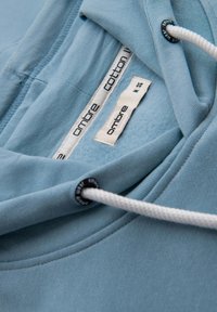 Felpa in cotone azzurro chiaro con texture morbida, dotata di cappuccio con cordino, etichetta interna e dettagli di cucitura.