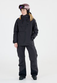 Svart isolerad skidjacka med fickor med dragkedja, i kombination med matchande byxor. Hjälmen är ljusrosa och har spegelglasögon.