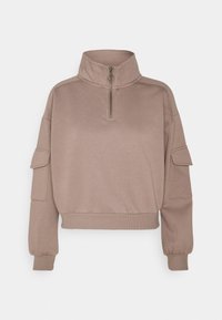 Jasnobrązowy pulower z półzamkiem przy kołnierzu. Posiada prążkowany dół i mankiety, boczne kieszenie oraz luźny krój. Gładka tekstura na całej powierzchni.