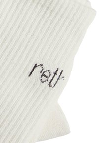 Chaussettes blanches côtelées en matériau doux, avec un petit logo brodé sombre sur un côté. Design simple et texturé.