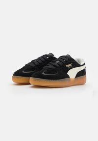 Sneaker in suede nero con logo bianco, caratterizzate da una punta liscia, lacci tondi e suola in gomma traslucida color nocciola.