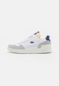 Baskets en cuir blanc avec accents en daim gris, design perforé, bout rond et un languette de talon bleue et jaune. Logo Lacoste sur le côté.