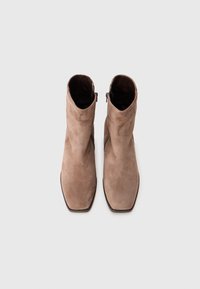 Botine maro din suede, cu vârf pătrat. Au fermoar pe lateral și o textură netedă. Design minimalist și linii curate.