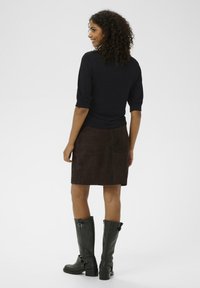 Black short-sleeve top, brown suede skirt, and knee-high black leather boots with buckles. Model shown from the back on a plain background.