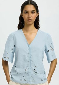 Blusa azzurra chiara con scollo a V, maniche corte con dettagli ricamati e orlo scallopato, realizzata in un tessuto testurizzato.
