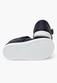 Scarpa in pelle blu con chiusura a cinturino, suola in gomma bianca con texture rigata, mostra la parte inferiore con dettagli del motivo.