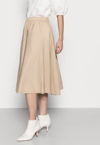 Beige, knie-lange rok gemaakt van lichtgewicht stof met een elastische tailleband. Draagt met witte, spitse enkelboots.