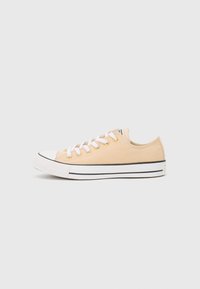 Canvas sneakers i lys beige med hvite snøre og øyer. Har en hvit gummitopp og en såle med svart stripe. Lågt topp-design.