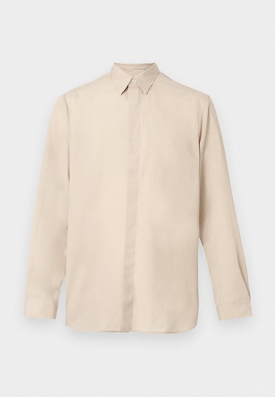 Μπεζ μακρυμάνικο πουκάμισο από απαλό ύφασμα, με γιακά με κουμπιά, πλήρη εμπρόσθια πατιλέτα και ίσια κάτω ραφή. Στρογγυλεμένα μανίκια.