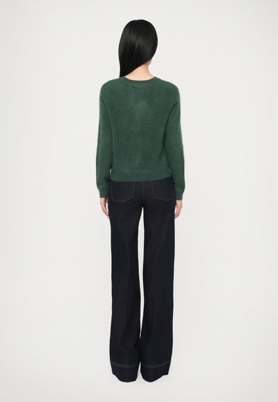 Groene gebreide trui met textuurpatroon, lange mouwen, ronde hals, gecombineerd met donkerblauwe flared jeans met achterzakken en contrasterende stiksels.