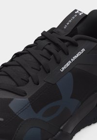 Κοντινό πλάνο μαύρου αθλητικού παπουτσιού Under Armour με υφασμένα κορδόνια και λογότυπο στο πλάι και στην γλώσσα που αναγράφει "REACT XT".