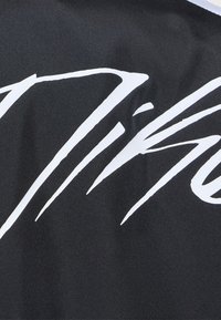 Gros plan de tissu noir avec de grandes lettres blanches en cursive ou en écriture manuscrite partiellement visibles.