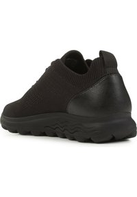 Scarpa sportiva nera con tomaia in maglia testurizzata e pannello posteriore in pelle liscia, dotata di una suola in gomma spessa e ondulata per un maggiore supporto.