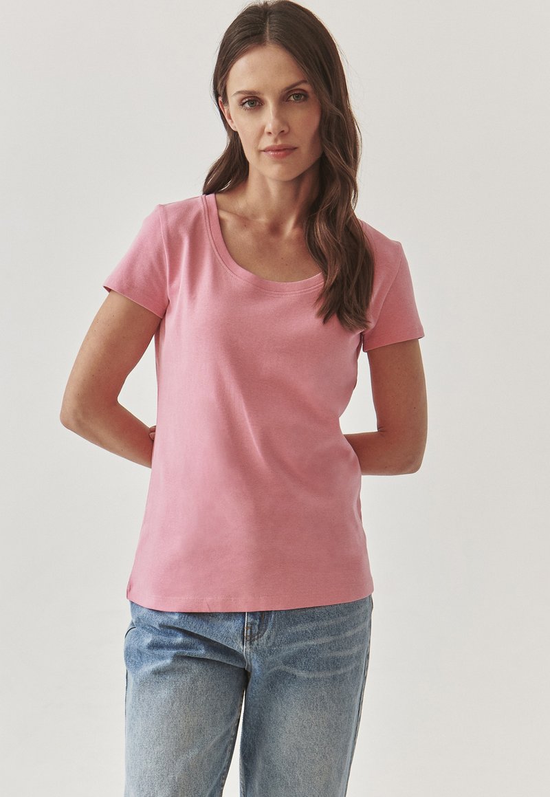 Lys pink, T-shirt med kortærmer og rund halsudskæring, lavet af blødt bomuld. Sammen med lyseblå denimjeans. Simpelt, tætsiddende design.