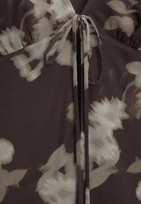 Kukallinen mekko tumman taupen sävyssä, kevyestä kankaasta, jossa on solmittava sulkija kaula-aukossa ja virtaava siluetti.