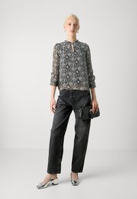 Blusa trasparente a fantasia con scollo rotondo e dettaglio a chiave, abbinata a jeans scuri a vita alta e scarpe con tacco a blocco argentate.