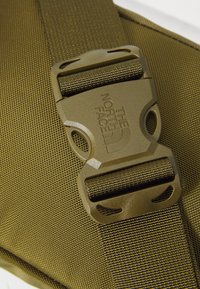 Zielony oliwkowy nylonowy pasek z plastikową klamrą z logo "The North Face", prezentujący teksturowany materiał i mocne detale obszycia.