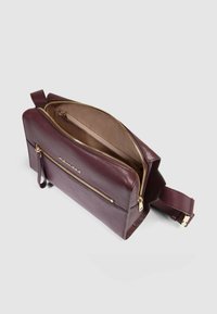 Bolso de cuero burdeos con cremallera dorada, forma estructurada y correa ajustable. El interior incluye un bolsillo con cremallera y forro beige.