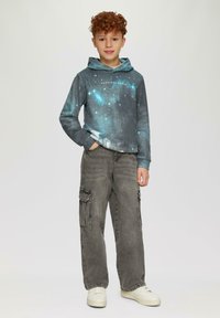 Kapuzensweatshirt mit einem weltraumthemen Muster in dunkelgrau und blau, kombiniert mit lockeren grauen Cargo-Hosen und weißen Sneakers.