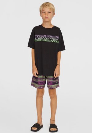 Svart T-shirt med stor grön och lila text; flerfärgade shorts med lila, grön och svarta ränder; svarta tofflor.