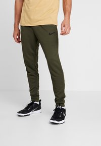 Gröna Nike-svettsbyxor med smal passform, elastiska benslut och sidofickor, i kombination med en ljusgul T-shirt och svarta träningsskor.