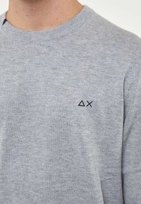 Maglione grigio a maglia con scollo rotondo, texture sottile e un piccolo logo blu navy sul lato sinistro del petto.