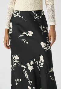 Jupe noire à fleurs avec une texture lisse, des motifs floraux abstraits crème et une taille ajustée, adaptée à diverses occasions.