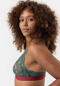 Groene kant bralette met bloemmotief, voorzien van een rode band en verstelbare bandjes. Zachte textuur met een driehoekige cupvorm.