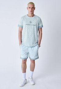 T-shirt bleu clair à manches courtes avec motif géométrique et inscription "PROJECT X PARIS", assorti à un short et des baskets blanches.
