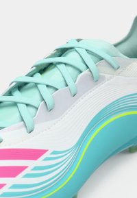 Ανοιχτό μπλε ποδοσφαιρικό παπούτσι με λευκή μεσαία περιοχή, με υφασμένους τόνοι και ροζ ρίγες. Οι κορδόνια και το σχέδιο αναδεικνύουν δυναμική κίνηση.