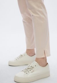 Ροζ ανοιχτό ροζ παντελόνι με ευθεία κοπή και πλαϊνή σχισμή στο τελείωμα, συνδυασμένο με λευκά αθλητικά παπούτσια με υφή και επίπεδη σόλα.