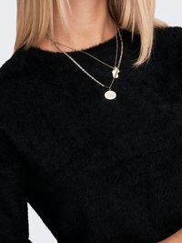 Black, fluffy sweater with a round neckline. Three layered gold necklaces with various pendants: oval, textured disc, and flat charm.