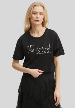 T-shirt nera in cotone con maniche corte e scollatura rotonda, decorata con una lavorazione di strass che riporta la scritta "Twisted Attitude" in corsivo.