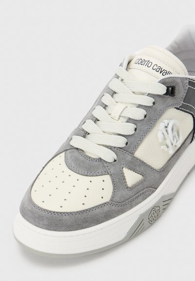 Sneaker bianca e grigia in pelle e suede con punta perforata, lacci bianchi e logo impresso sul lato e sulla linguetta.