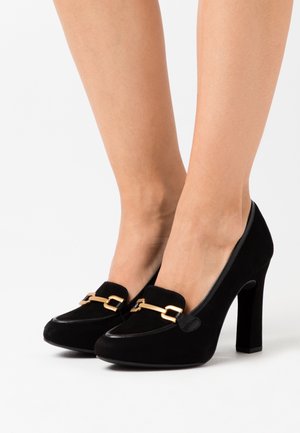 Chaussures à talons hauts en suède noir avec un accent en chaîne dorée, bout arrondi et texture lisse. Le talon bloc offre de la stabilité.