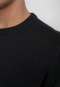 Donker gebreide trui met een ronde hals. De stof lijkt zacht met een gladde textuur. De kleur is diep marineblauw, met minimale details.