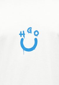 Μπλε κείμενο σε στυλ γκράφιτι σε λευκό ύφασμα γράφει "H G O" με ένα μεγάλο χαμόγελο σε σχήμα U από κάτω, όλα με σταγόνες μπογιάς.