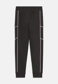 Zwarte sweatpants met witte piping-details langs de zijkanten, elastische tailleband en geribde boorden bij de enkels. Gladde stoffen textuur.