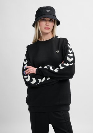Sort sweatshirt med hvide chevronmønstre på ærmerne, med et lille logo på brystet. Kombineret med en sort bøttehat.