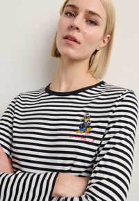 Black and white striped long-sleeve shirt featuring an embroidered cartoon character and red text on the chest. Cotton material, round neckline.
